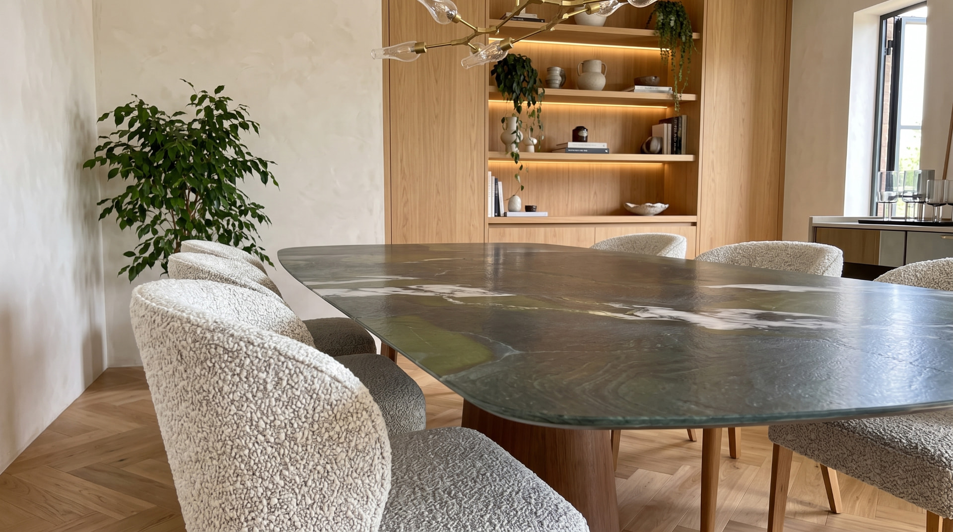Mesa de jantar em pedra verde com cadeiras bouclé e estante de madeira iluminada