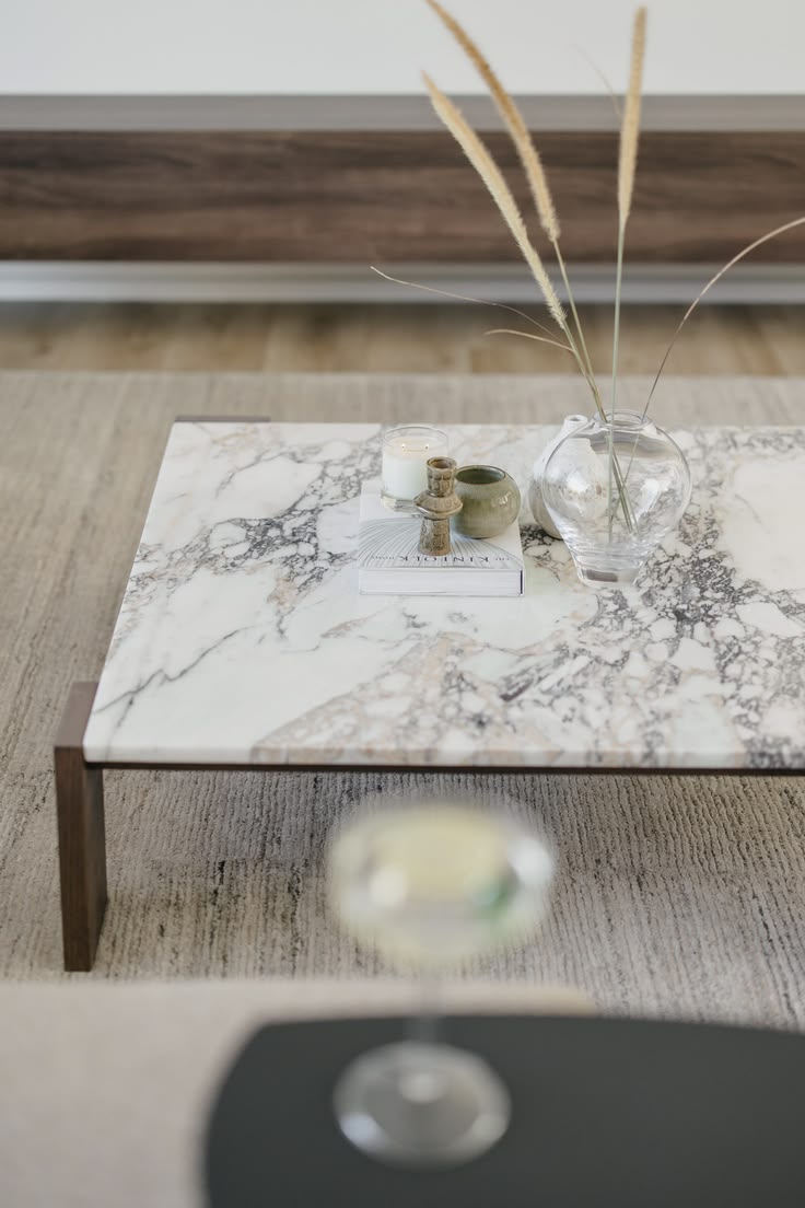 Mesa de centro em mármore claro com veios grisalhos e mauve, base de madeira escura, em sala de estar